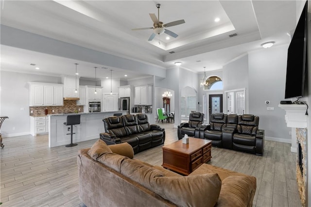 living room featuring crown molding, a fireplace, a tray ceiling, and ceiling fan with notable chandelier