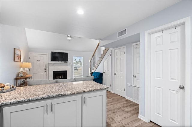 kitchen with light stone counters, a fireplace, white cabinets, and light wood-type flooring