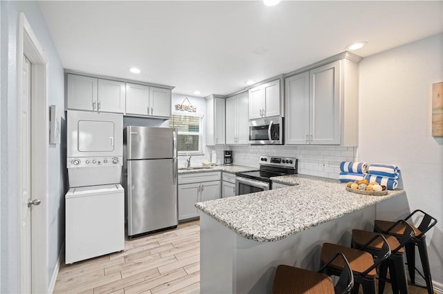 kitchen with stacked washer and dryer, light hardwood / wood-style flooring, appliances with stainless steel finishes, a kitchen breakfast bar, and kitchen peninsula