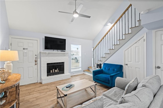 living room featuring lofted ceiling, a fireplace, ceiling fan, and light wood-type flooring