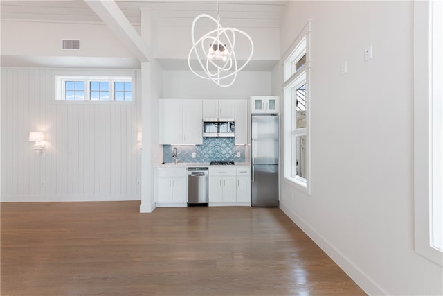 kitchen featuring stainless steel appliances, an inviting chandelier, hanging light fixtures, wooden walls, and white cabinetry