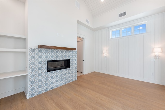 unfurnished living room featuring built in shelves, a fireplace, light hardwood / wood-style floors, and high vaulted ceiling