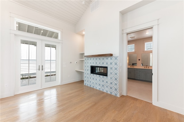 unfurnished living room featuring a fireplace, wood ceiling, light wood-type flooring, and french doors