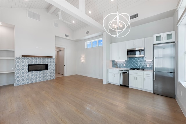 kitchen with stainless steel appliances, high vaulted ceiling, hanging light fixtures, white cabinets, and light wood-type flooring