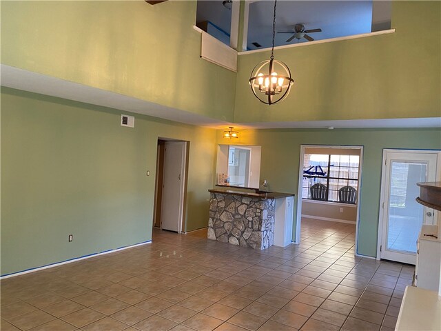 interior space with light tile patterned floors, ceiling fan with notable chandelier, and a high ceiling