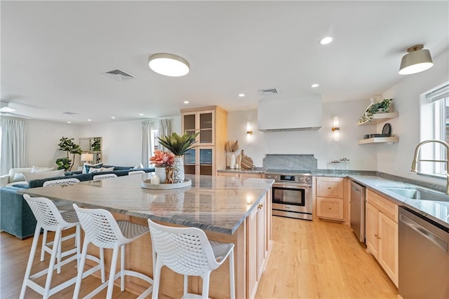 416 E Ave C Ave, Port Aransas, TX 78373 - kitchen with appliances with stainless steel finishes, light brown cabinets, a sink, light wood-style floors, and a kitchen breakfast bar