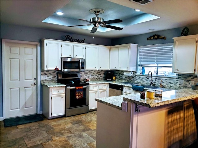 kitchen with appliances with stainless steel finishes, a peninsula, ceiling fan, backsplash, and a sink
