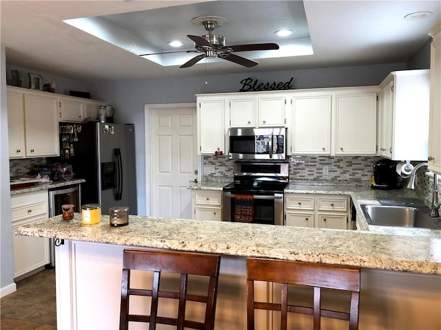 kitchen featuring stainless steel appliances, a sink, a peninsula, ceiling fan, and backsplash