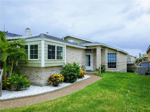 view of front of house featuring brick siding, a front lawn, central AC unit, and a chimney