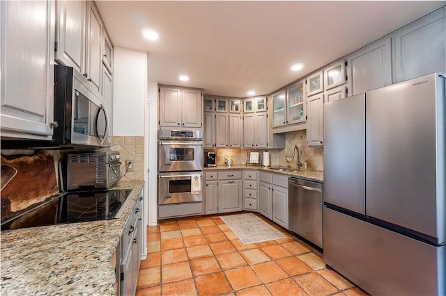 kitchen with stainless steel appliances, tasteful backsplash, light stone countertops, and sink