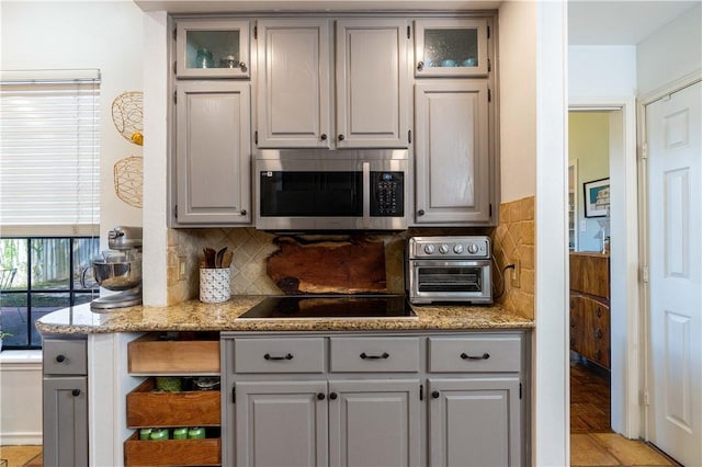 kitchen featuring gray cabinets, light stone countertops, black electric stovetop, and backsplash