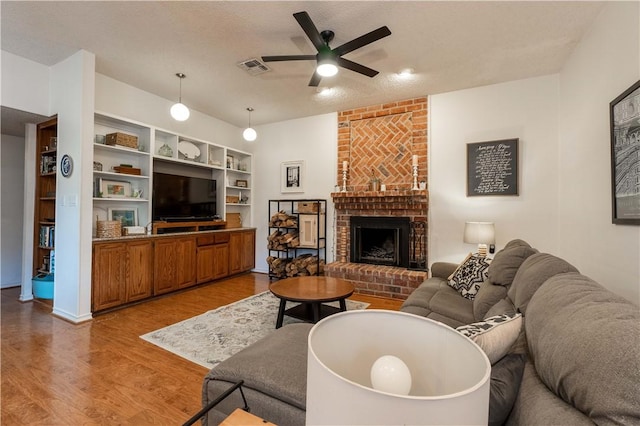 living room with a brick fireplace, a textured ceiling, light hardwood / wood-style floors, and ceiling fan