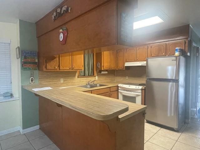 kitchen with sink, light tile patterned floors, stainless steel fridge, kitchen peninsula, and white range with electric cooktop