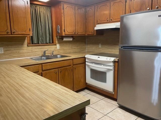 kitchen with white range with electric stovetop, stainless steel refrigerator, tasteful backsplash, sink, and light tile patterned floors