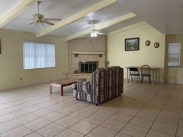 living room with vaulted ceiling with beams, light tile patterned floors, a fireplace, and ceiling fan