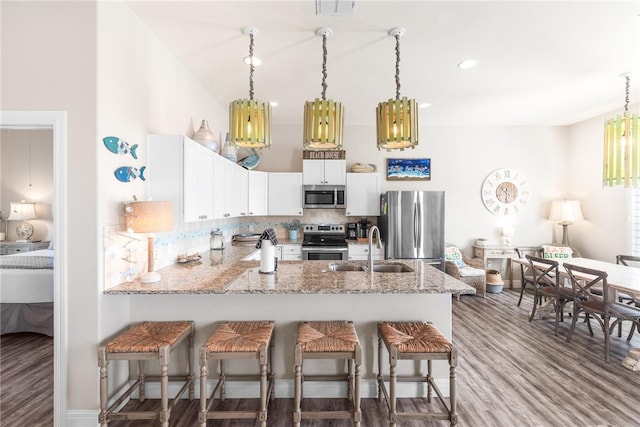 kitchen with wood-type flooring, kitchen peninsula, light stone countertops, white cabinetry, and appliances with stainless steel finishes