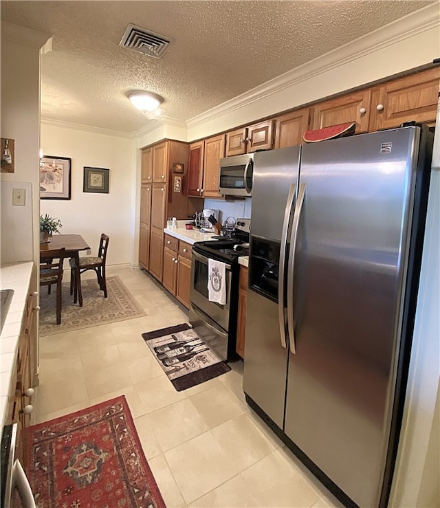 kitchen with stainless steel appliances, tile countertops, light tile patterned flooring, ornamental molding, and a textured ceiling