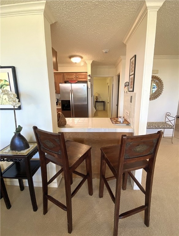 kitchen with tile countertops, a textured ceiling, crown molding, and stainless steel fridge with ice dispenser