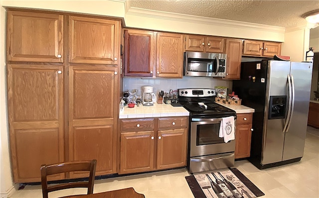 kitchen featuring ornamental molding, stainless steel appliances, backsplash, a textured ceiling, and tile countertops