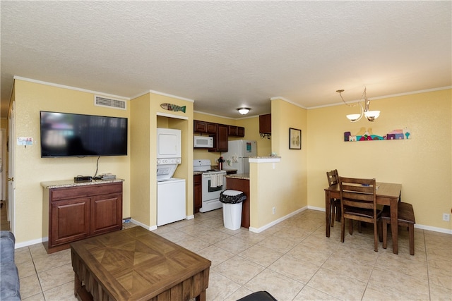 tiled living room featuring a textured ceiling, stacked washer / dryer, a notable chandelier, and ornamental molding