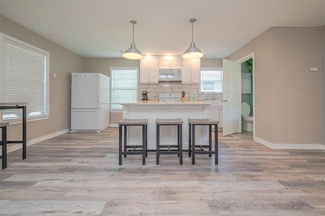 kitchen with light stone countertops, white cabinetry, hanging light fixtures, a kitchen breakfast bar, and white appliances