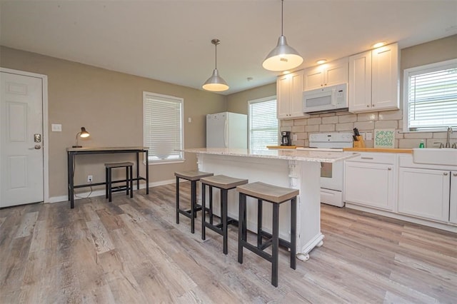 kitchen with tasteful backsplash, white appliances, a center island, white cabinetry, and hanging light fixtures