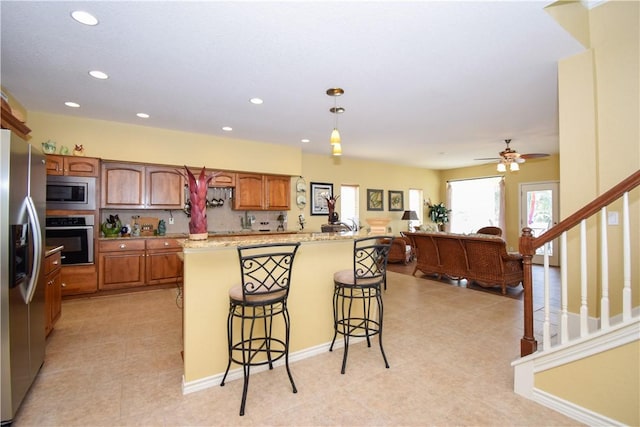 kitchen featuring hanging light fixtures, appliances with stainless steel finishes, brown cabinetry, open floor plan, and a kitchen bar