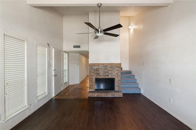 unfurnished living room featuring a fireplace, visible vents, a towering ceiling, a ceiling fan, and wood finished floors