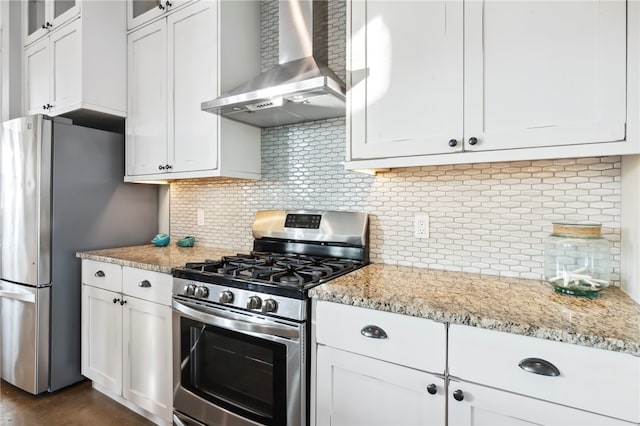 kitchen featuring light stone counters, white cabinetry, wall chimney range hood, appliances with stainless steel finishes, and decorative backsplash