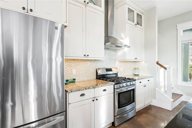 kitchen with wall chimney range hood, appliances with stainless steel finishes, light stone countertops, decorative backsplash, and white cabinets