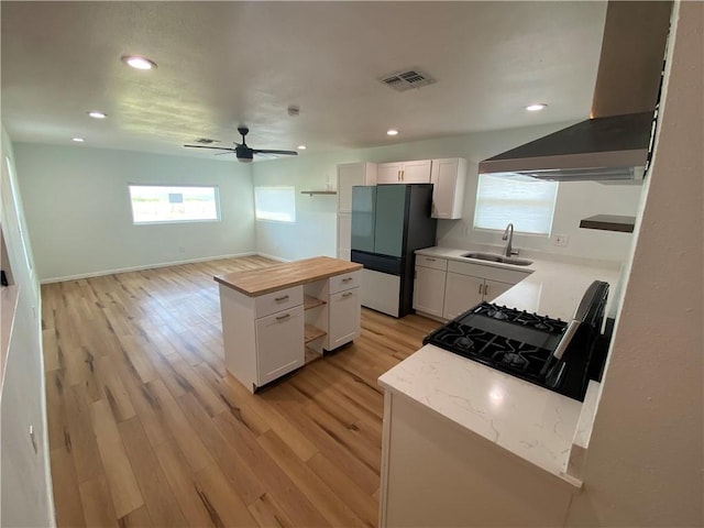 kitchen with freestanding refrigerator, wall chimney range hood, range with gas cooktop, a sink, and light wood finished floors