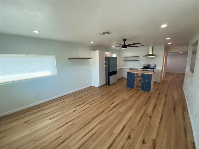 kitchen with wall chimney range hood, ceiling fan, visible vents, refrigerator with ice dispenser, and stainless steel range oven