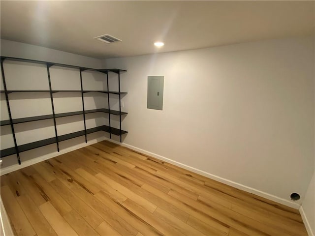 finished basement featuring light wood-style floors, baseboards, electric panel, and visible vents