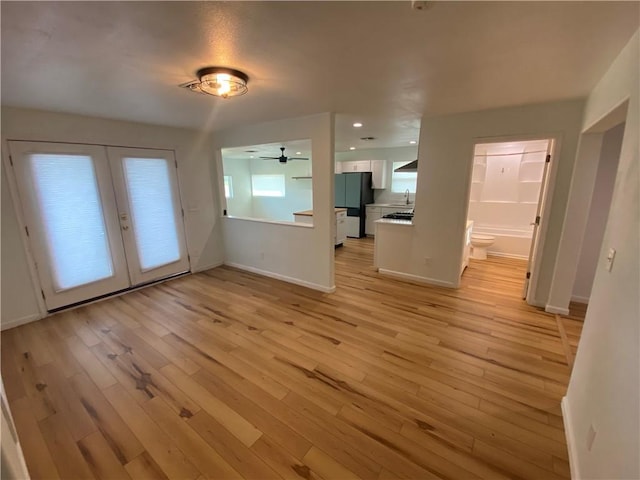 interior space featuring baseboards, a ceiling fan, french doors, and light wood-type flooring