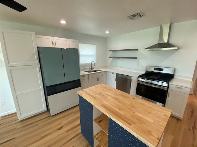 kitchen featuring appliances with stainless steel finishes, open shelves, wall chimney exhaust hood, a sink, and butcher block countertops