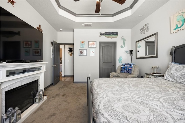 bedroom with visible vents, a tray ceiling, ornamental molding, a premium fireplace, and carpet flooring