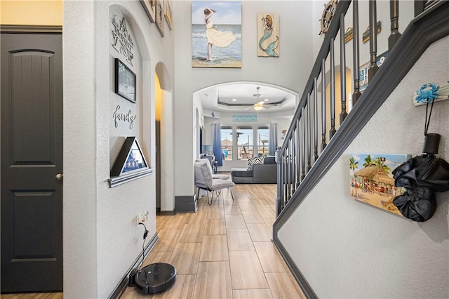 foyer with arched walkways, stairs, a raised ceiling, and baseboards