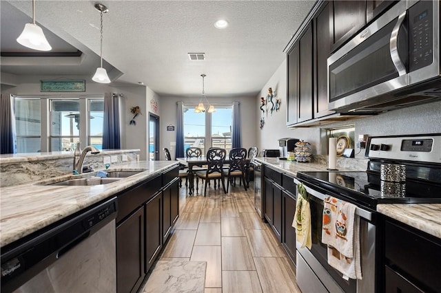 kitchen featuring visible vents, light stone countertops, a textured ceiling, stainless steel appliances, and a sink