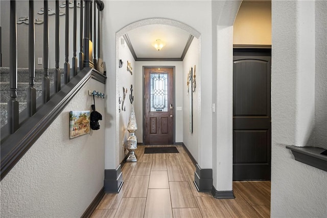 entryway featuring ornamental molding, wood finished floors, arched walkways, baseboards, and a textured wall