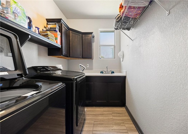 washroom with baseboards, a textured wall, cabinet space, a sink, and washing machine and dryer