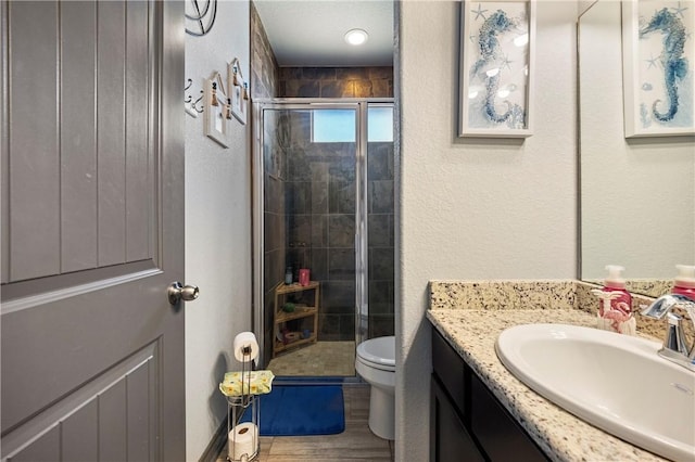 bathroom with a shower stall, toilet, wood finished floors, a textured wall, and vanity