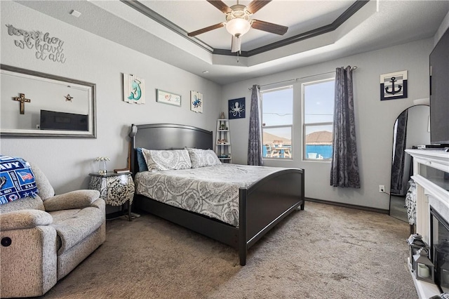 carpeted bedroom with a glass covered fireplace, a raised ceiling, a ceiling fan, and baseboards