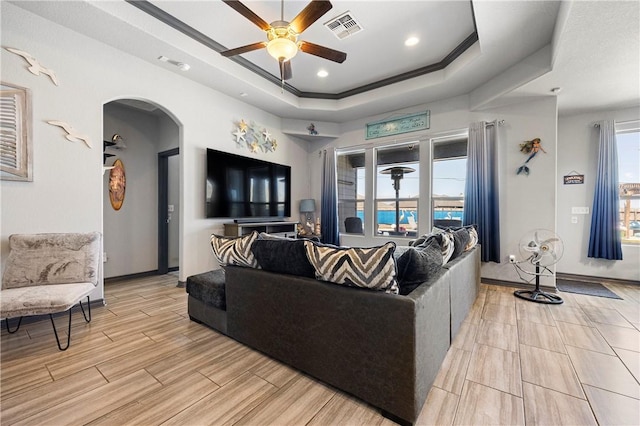 living area featuring a ceiling fan, visible vents, wood tiled floor, arched walkways, and a raised ceiling