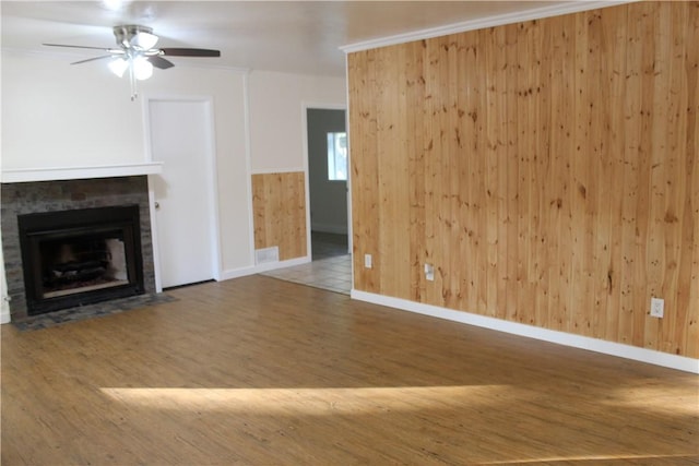 unfurnished living room with hardwood / wood-style flooring, ornamental molding, ceiling fan, and wood walls