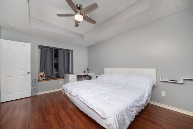 bedroom with ceiling fan, a tray ceiling, dark hardwood / wood-style flooring, and a textured ceiling