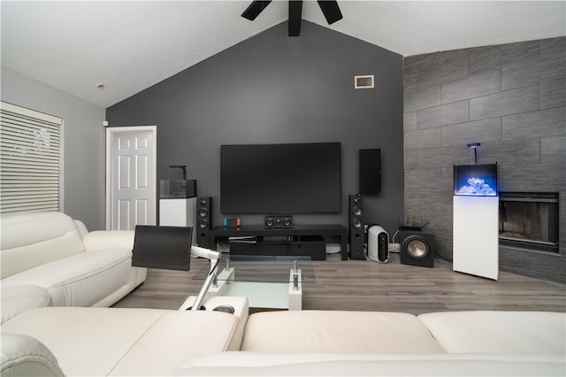 living room featuring light wood-type flooring, vaulted ceiling, ceiling fan, and a tiled fireplace