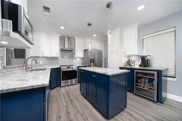 kitchen featuring wall chimney exhaust hood, stainless steel appliances, beverage cooler, pendant lighting, and a center island