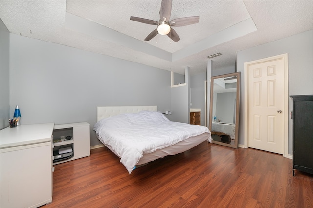 bedroom with a tray ceiling, ceiling fan, dark hardwood / wood-style flooring, and a textured ceiling