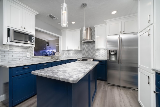 kitchen with blue cabinetry, a center island, wall chimney range hood, pendant lighting, and appliances with stainless steel finishes