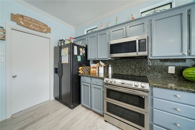 kitchen featuring light wood-type flooring, tasteful backsplash, dark stone counters, ornamental molding, and stainless steel appliances